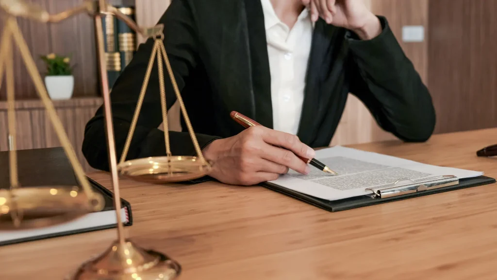 Lawyer signing documents with a scale of justice beside them